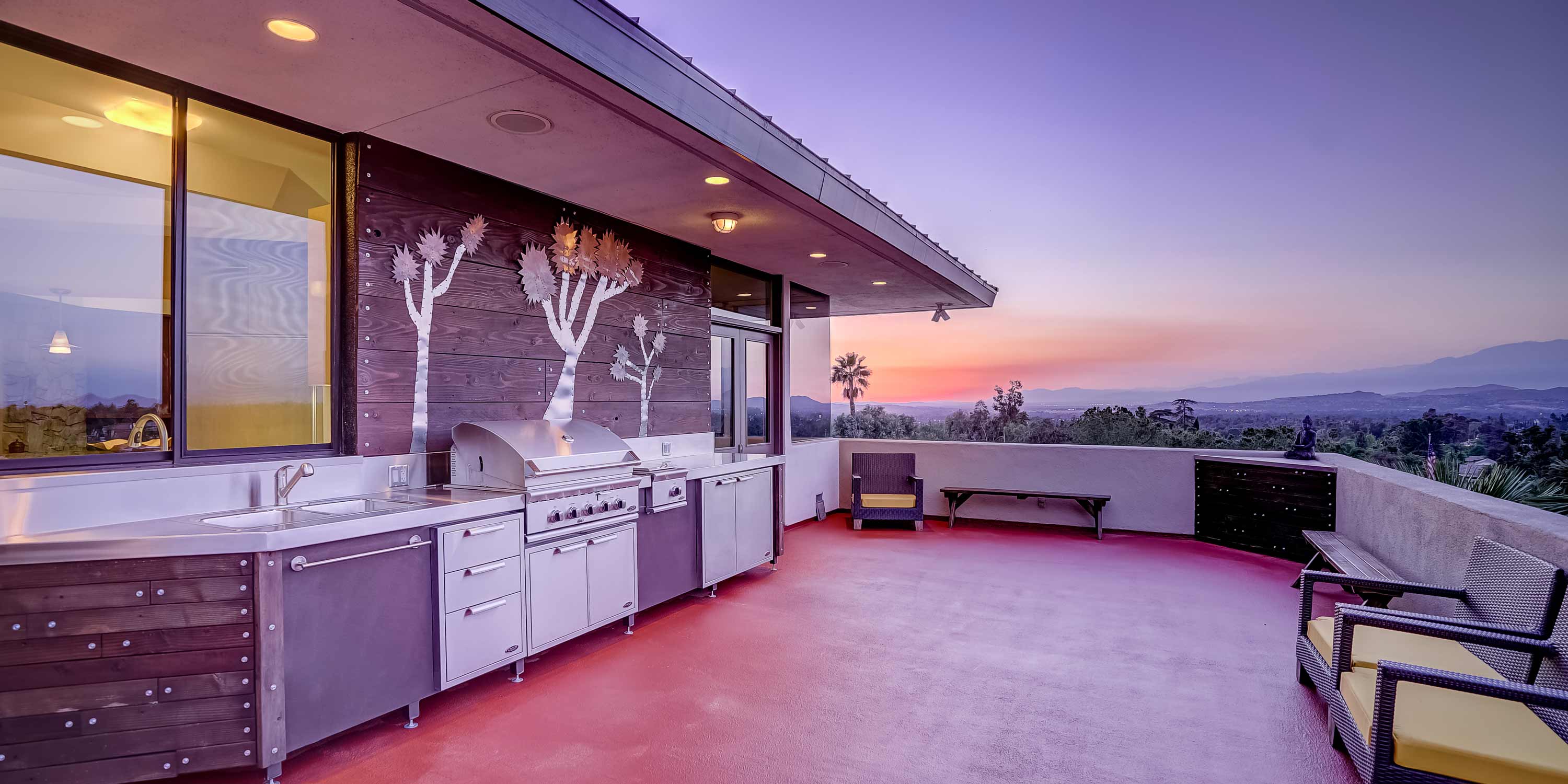 Modern outdoor kitchen and patio with stainless steel appliances and sunset mountain views.