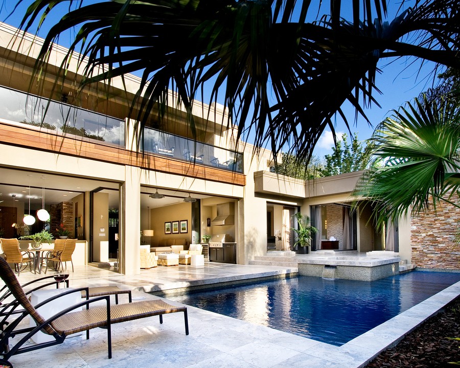 A luxurious modern home with an open floor plan leading to an elegant outdoor patio featuring a swimming pool, lush greenery and stylish outdoor furniture.