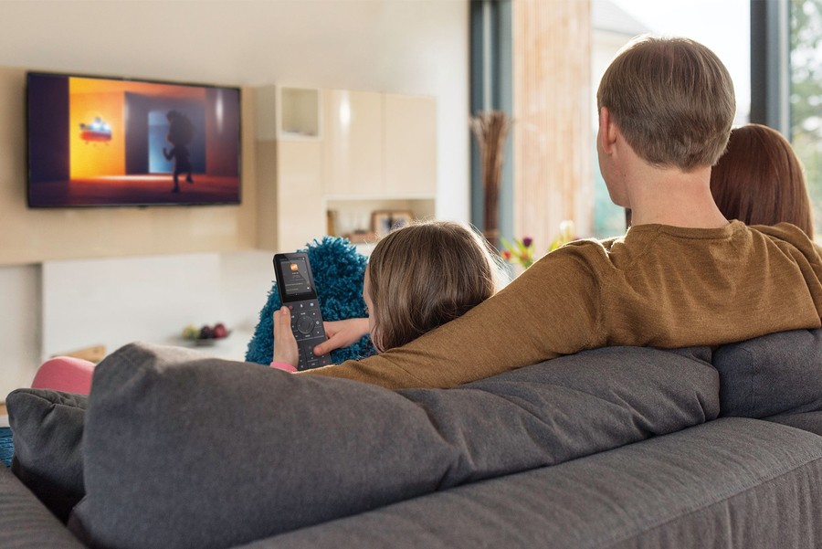 a family sits on a couch and one person holds a Crestron TSR-310 remote control.