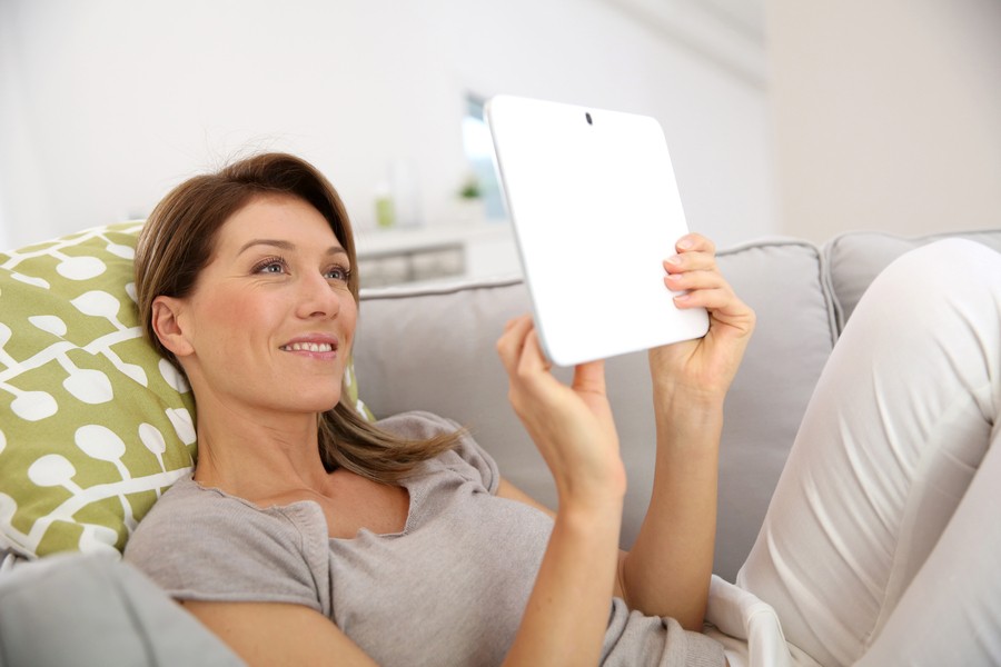 A woman relaxes on a couch, engaged with a tablet.