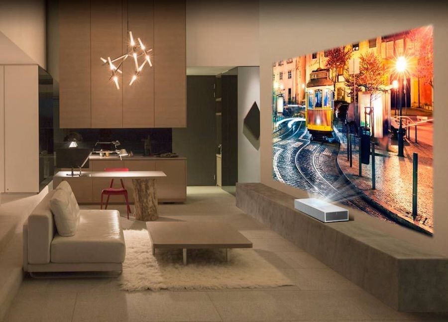 modern living room with upward-firing projector and projection screen in front of low-profile couch and table