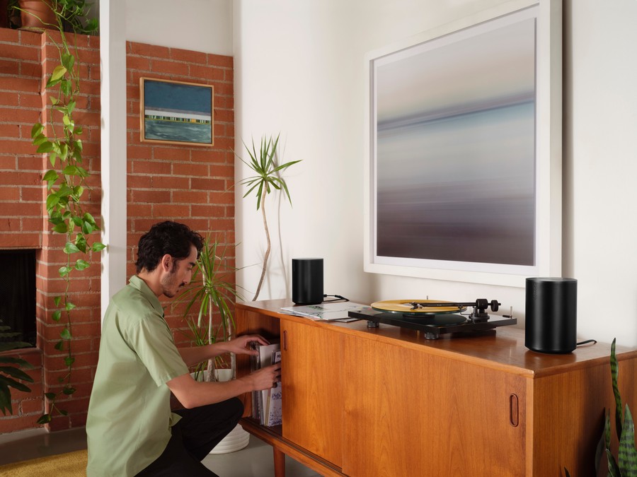 man kneeling in front of AV credenza with Sonos speakers sitting on top